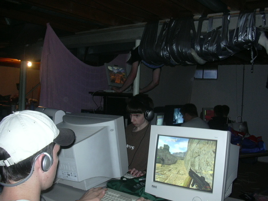 The original 2003 LAN party photograph: a gamer suspended in duct tape above friends playing on CRT monitors.
